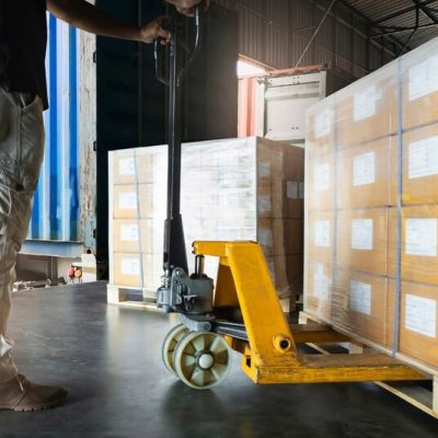Warehouse worker using a hand pallet truck to unload cargo pallets in a storage facility, emphasizing efficient material handling solutions for optimizing warehouse operations.
