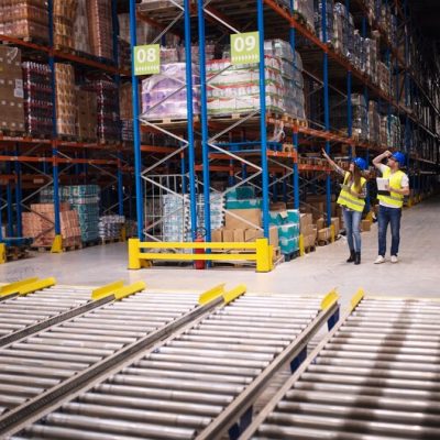 Warehouse workers inspecting inventory in a large storage facility, discussing pallet racking systems and organization, with shelves stocked with goods in Arlington, TX.